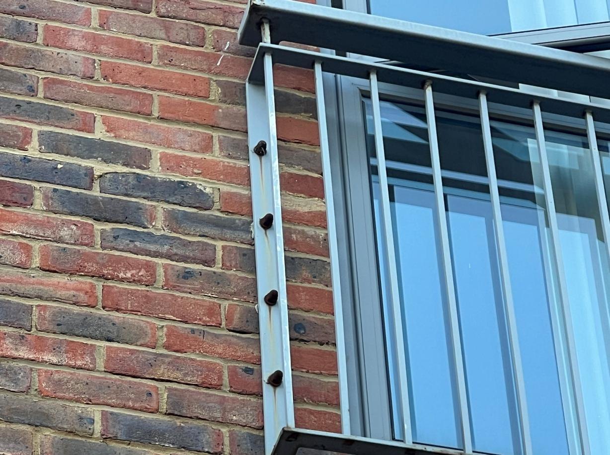 Metal guarding and its fixings beside brickwork.