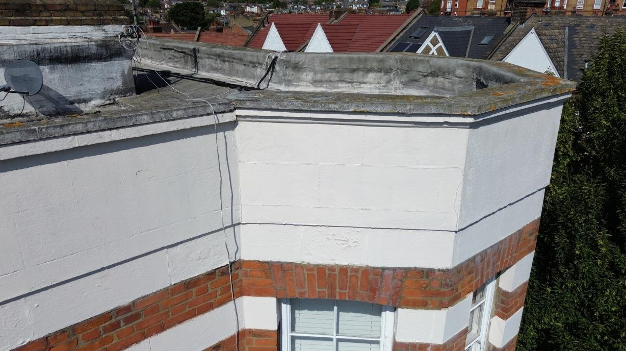 Roof covering and rendered parapet above a mansion-block window bay.