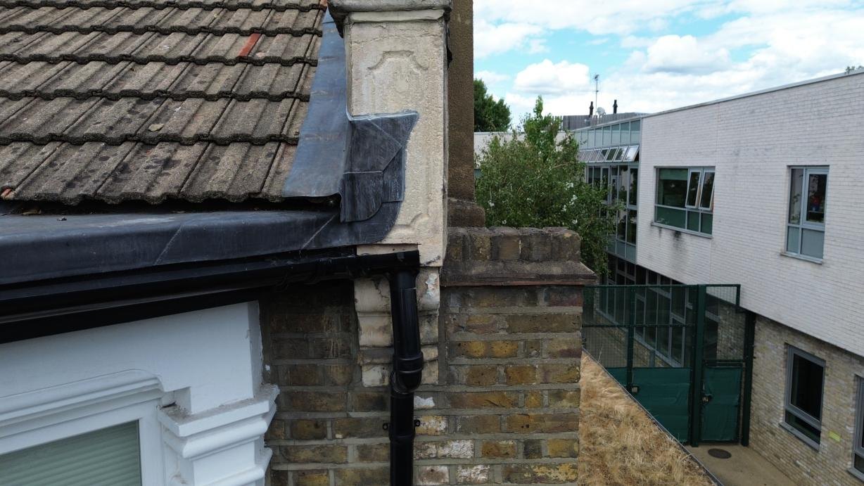 Parapet, flashing and rainwater-pipe junction above the bay window.